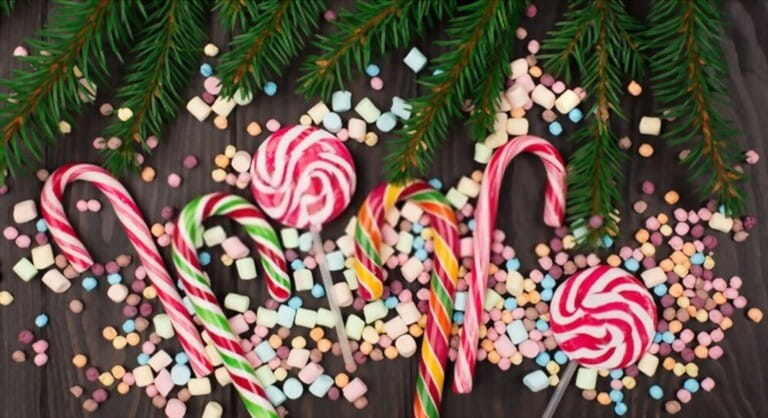 Colorful candies, lollypops, marshmallows, Candy canes and Fir Tree branches on dark wooden background. Top view, copy space. Holiday Christmas sweet concept.