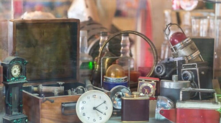 Assorted vintage items, clocks, cameras, flasks, sextant, lamps behind shop window. Assorted vintage items, clocks, cameras, flasks, sextant, lamps behind shop window.