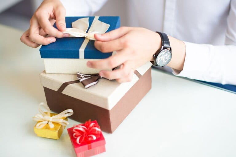 Close-up of gift wraper carefully wrapping and selecting stacked gift boxes placed on a white table Close-up of gift wraper carefully wrapping and selecting stacked gift boxes placed on a white table
