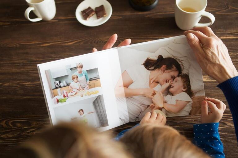 Senior woman and child hands holding a family photo album against background of a wooden table.