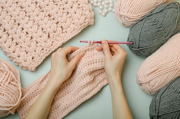 Crochet with your own hands.Knitting threads in pink and gray. Knitted scarf.Female hands hold a crochet hook and knit.DIY.Knitting rules. Creativity lessons.Winter activities during quarantine. Crochet with your own hands.Knitting threads in pink and gray. Knitted scarf.Female hands hold a crochet hook and knit.DIY.Knitting rules. Creativity lessons.Winter activities during quarantine.