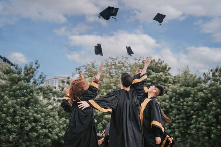 Asian students excitedly throw mortarboard into the air according to graduation day tradition