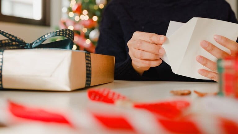 Close-up of woman's hand writing greeting cards with gift boxes on table at home Close-up of woman's hand writing greeting cards with gift boxes on table at home
