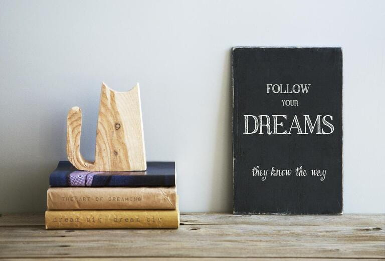 motivational quote FOLLOW YOUR DREAMS on chalkboard with books and wooden cat motivational quote FOLLOW YOUR DREAMS on chalkboard with books and wooden cat
