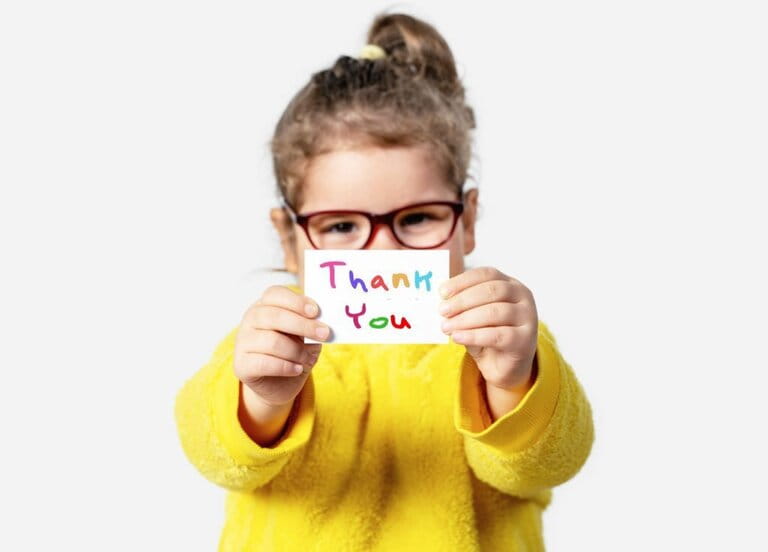 Adorable little girl holding a piece of paper with a Thank you note.