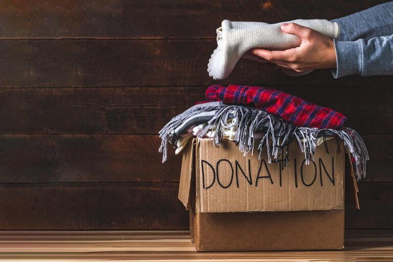 Donation concept. Donation box with donated clothes on wooden background. Charity. Help the poor and needy.
