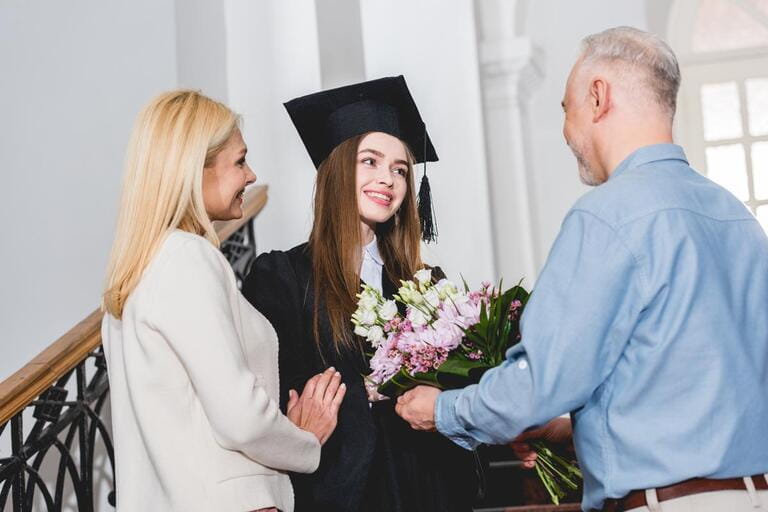 happy father giving flowers to cheerful daughter in graduation cap happy father giving flowers to cheerful daughter in graduation cap