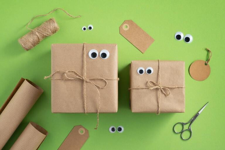 Funny gift boxes with eyes and wrapping materials. Jute rope, wrapping paper roll, scissors and gift tags on bright green background. Funny gift boxes with eyes and wrapping materials. Jute rope, wrapping paper roll, scissors and gift tags on bright green background.
