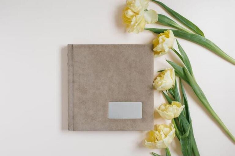 Beige family or wedding photo book and tulip flowers lie on a light beige background. Fond memories in photographs for memory Beige family or wedding photo book and tulip flowers lie on a light beige background. Fond memories in photographs for memory