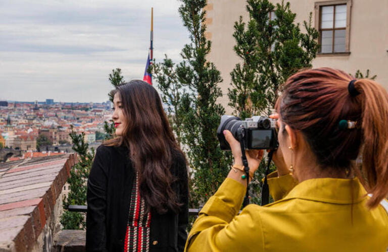 Woman taking side view photograph of friend, cityscape in background, Prague, Czech Republic Woman taking side view photograph of friend, cityscape in background, Prague, Czech Republic