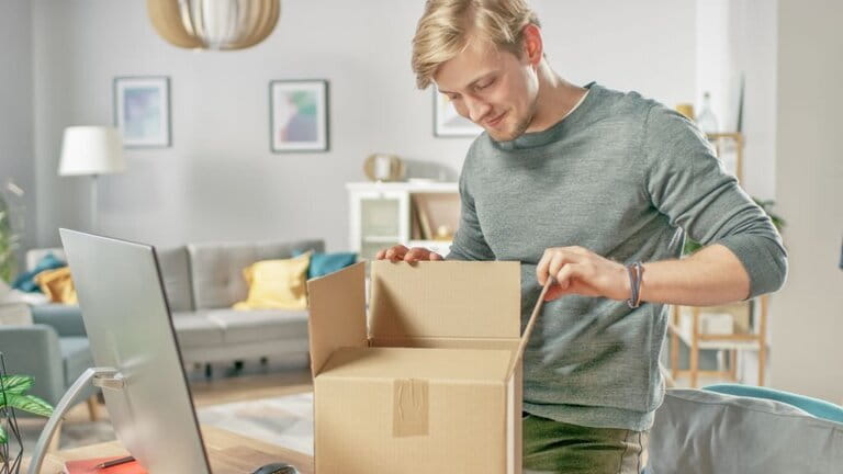 The handsome young man in the living room unpacked the cardboard box with interest