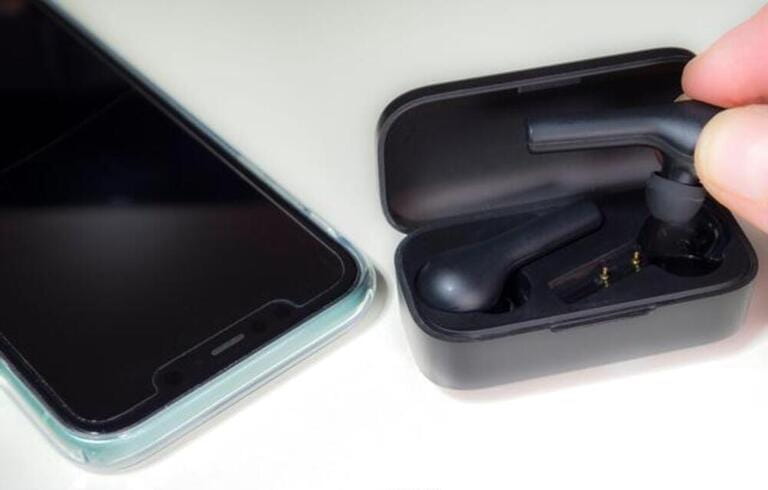 Closeup POV shot of fingers putting a pair of modern, battery operated, wireless earbuds / earphones into their charging case, next to a mobile phone. Closeup POV shot of fingers putting a pair of modern, battery operated, wireless earbuds / earphones into their charging case, next to a mobile phone.