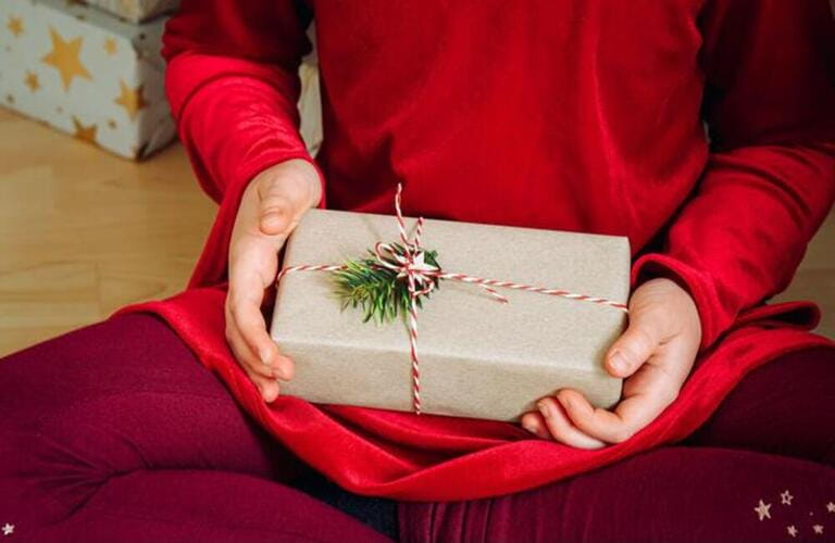 Close up view of girl child holding Christmas present in hands at home. Celebration