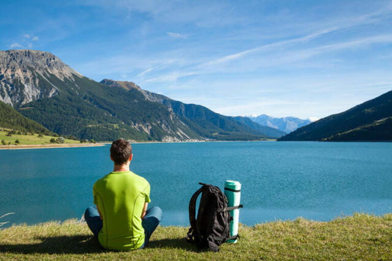 Hiker with backpack and rolled foam camping mattress looking at the lake with mountain background Hiker with backpack and rolled foam camping mattress looking at the lake with mountain background