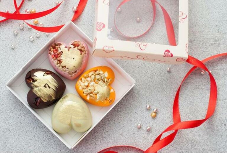 Gift box with heart shaped colored chocolate, decorated with red ribbon. Stone grey background Gift box with heart shaped colored chocolate, decorated with red ribbon. Stone grey background