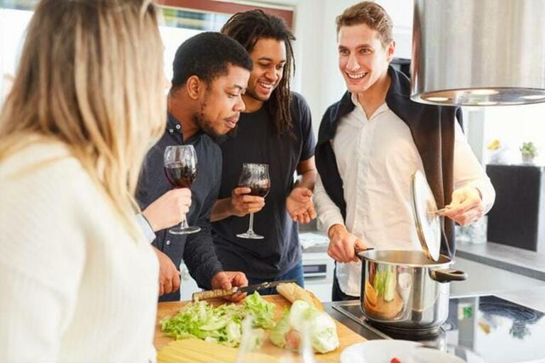 Friends cook lunch together in the kitchen with a glass of red wine Friends cook lunch together in the kitchen with a glass of red wine