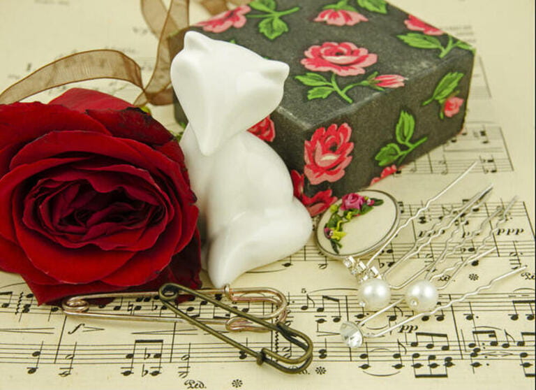 Still life with red rose and angel among several hairpins, gift boxes and buttons on the background of paper with notes Still life with red rose and angel among several hairpins, gift boxes and buttons on the background of paper with notes